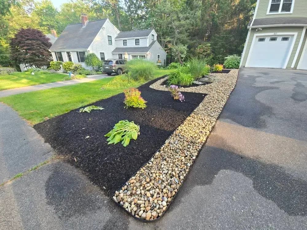 Mulched planting bed edged with river stone along a driveway