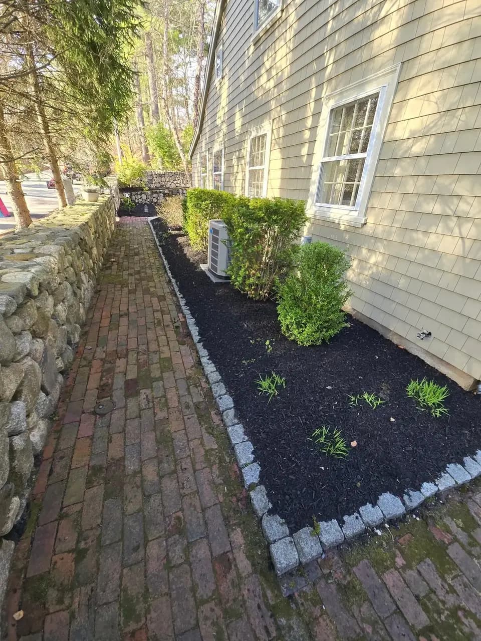 Side-yard mulch bed with stone edging beside a brick path