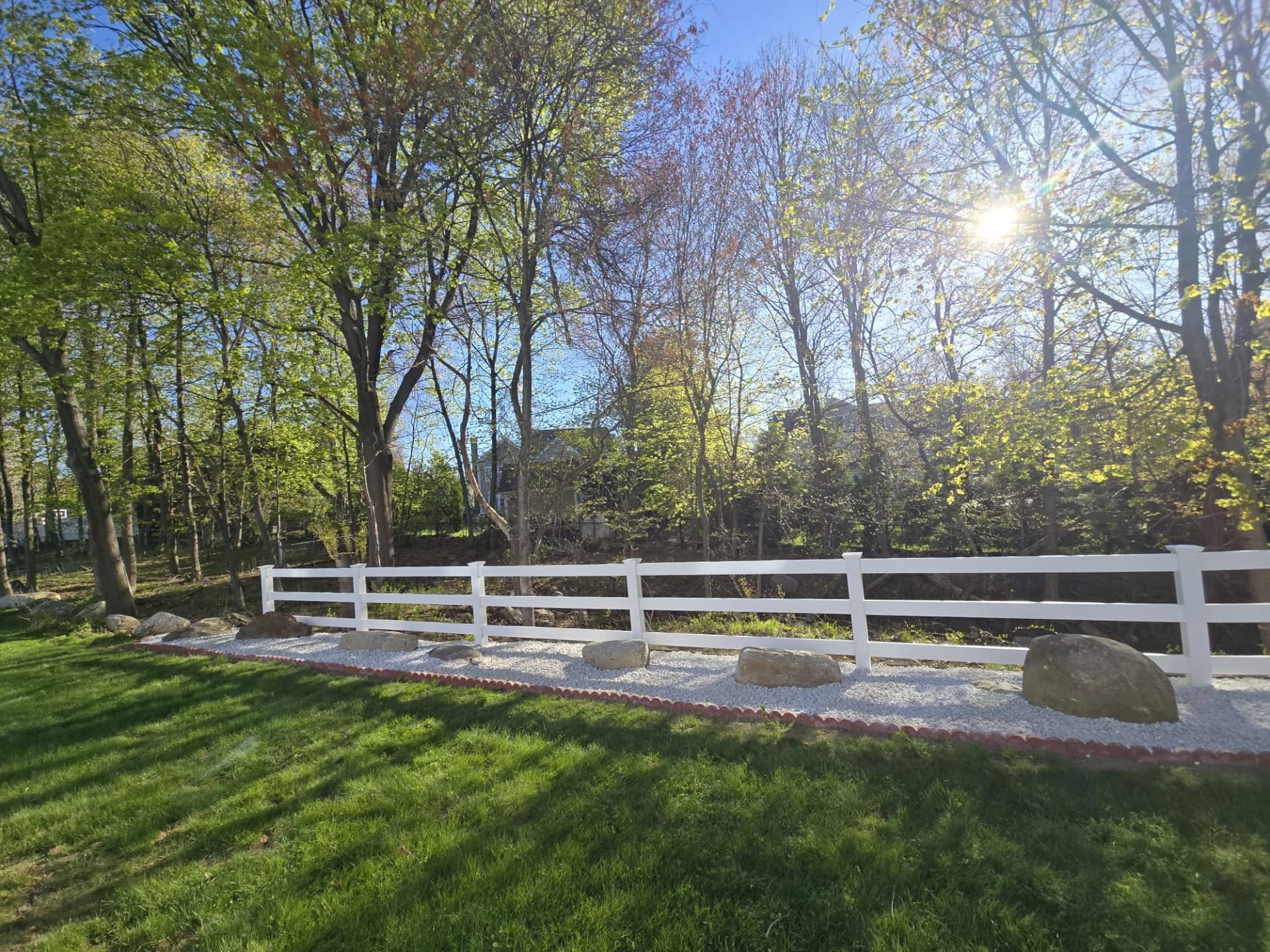 Cerca branca de três travessas junto à borda arborizada de um jardim em Shrewsbury, MA