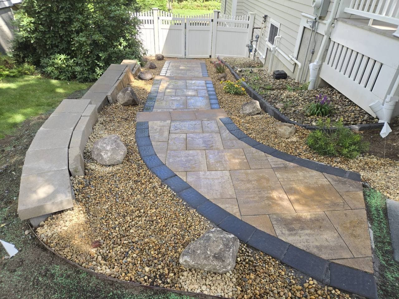 Sendero curvo con borde oscuro, grava y rocas decorativas en Needham, MA
