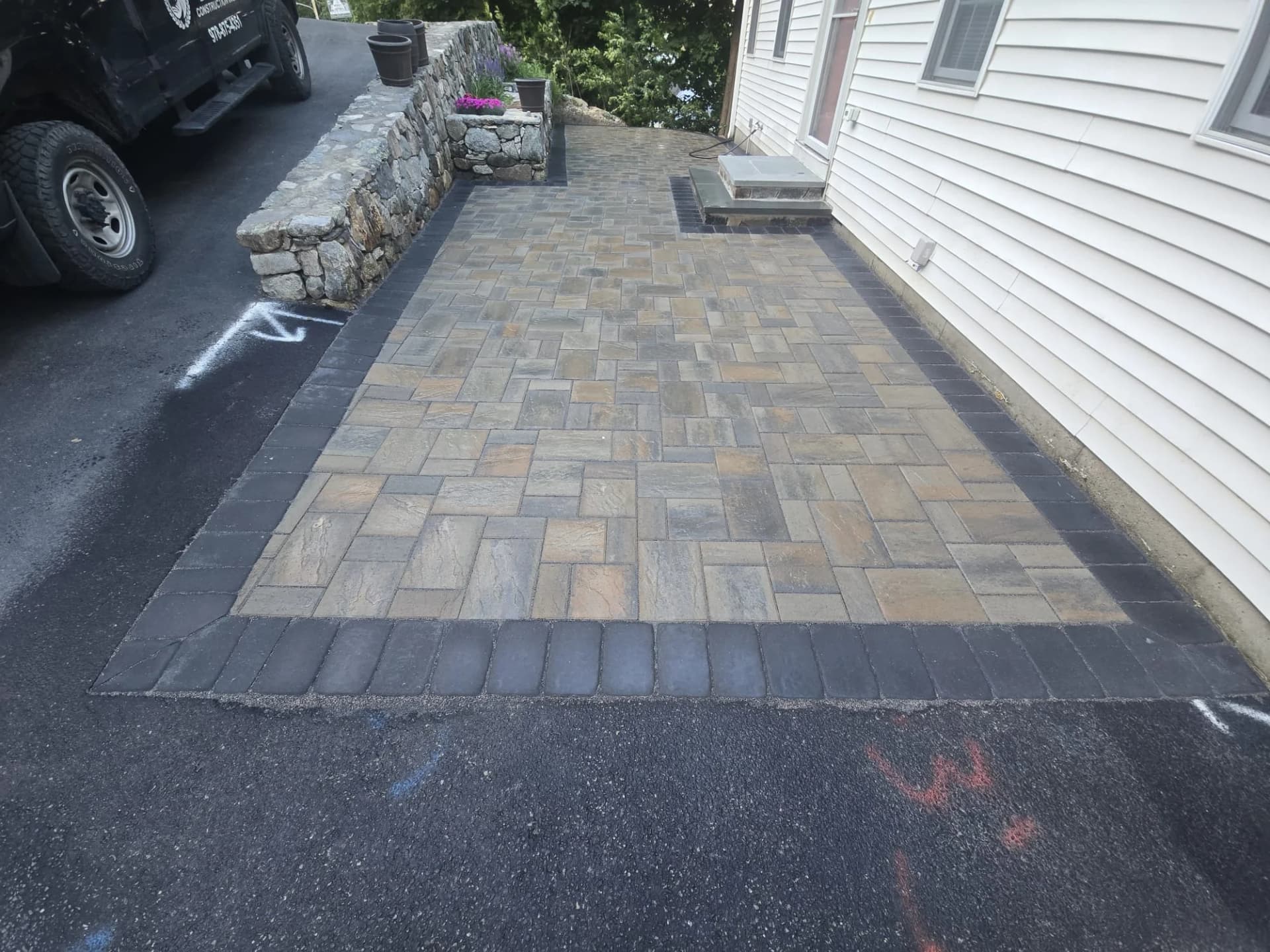 Paver patio with a dark border beside the house in Hudson, MA