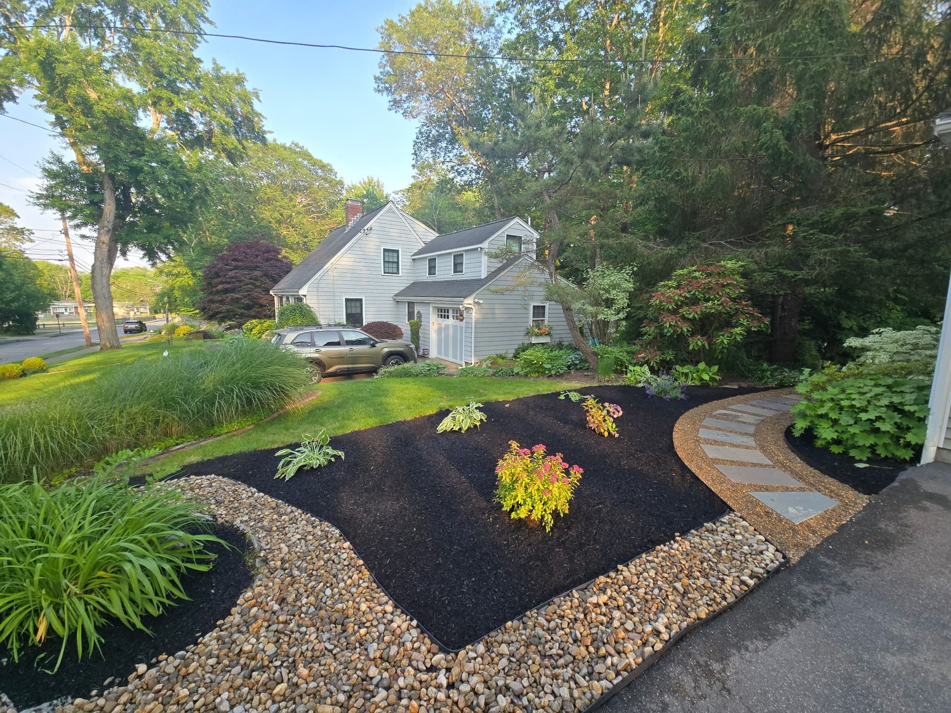 Front yard with fresh dark mulch beds, river-stone borders, and a stepping-stone path beside a gray house